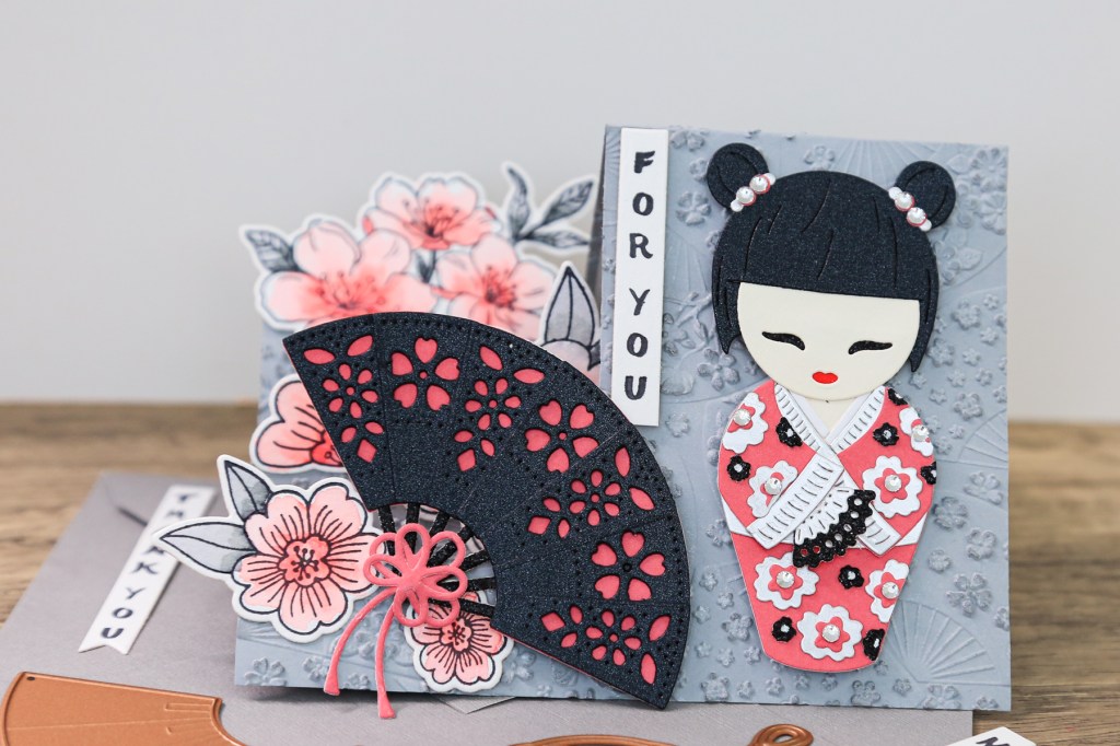 handmade card by Toni Chowdhury using the Spellbinders Spring in Kyoto collection featuring a Kokeshi doll, Japanese fan and cherry blossoms