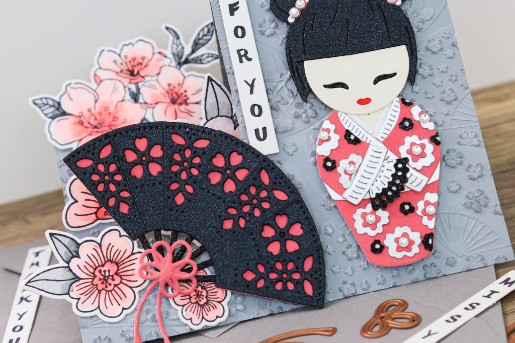 handmade card by Toni Chowdhury using the Spellbinders Spring in Kyoto collection featuring a Kokeshi doll, Japanese fan and cherry blossoms in black, grey and pink