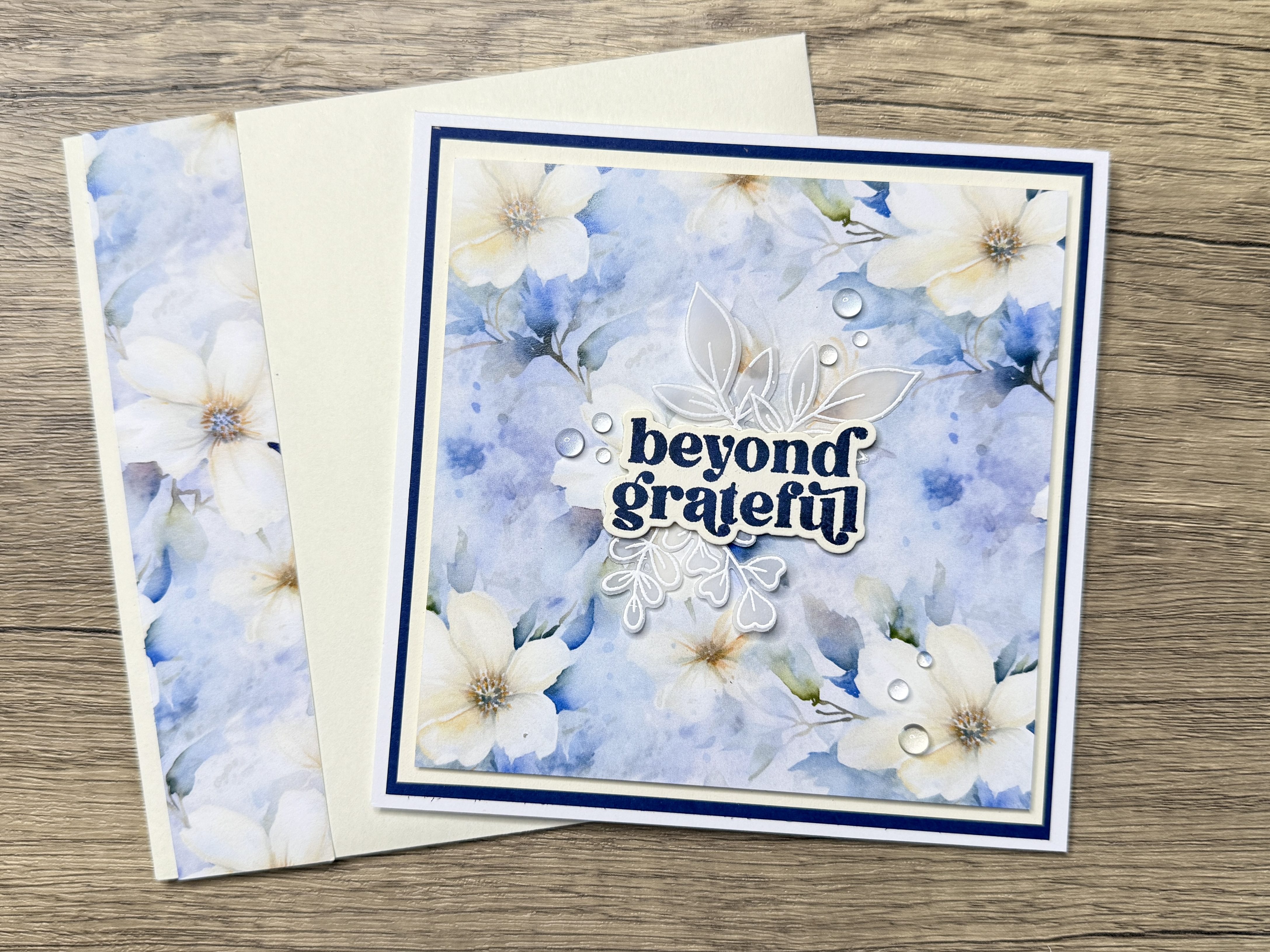 Handmade square card featuring floral patterned paper in shades of blue, cream and white, with a sentiment that reads 'beyond grateful' and decorative elements.
