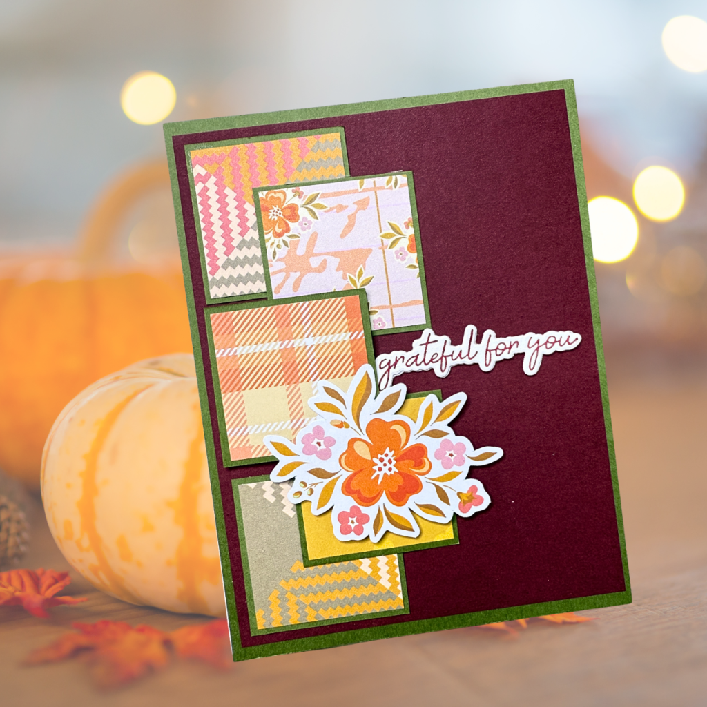 A handmade card featuring a maroon background with multiple squares of patterned papers in various colors and designs, adorned with a floral arrangement and the sentiment 'grateful for you.'