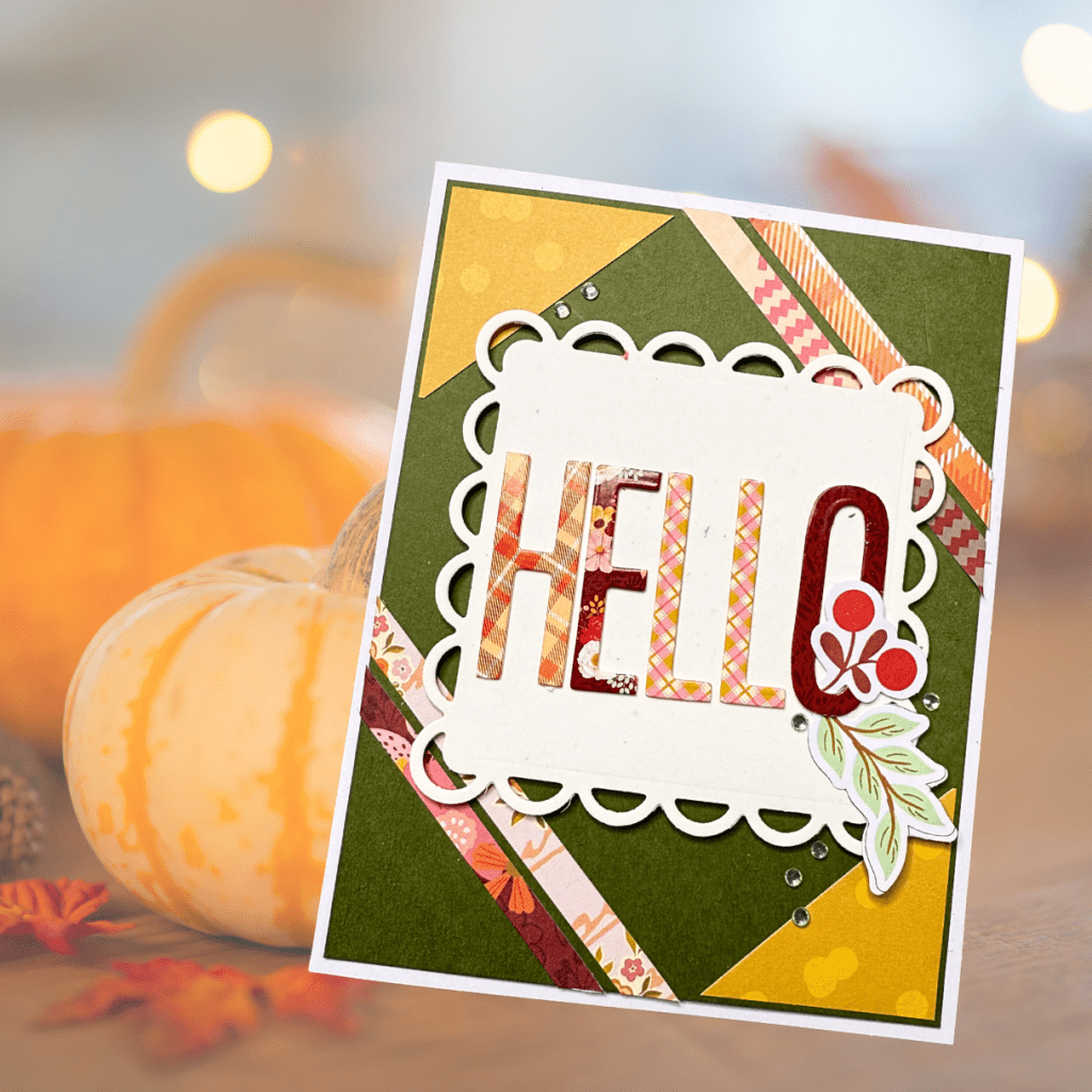 A handcrafted card featuring the word 'HELLO' made from patterned paper, surrounded by decorative elements like leaves and berries. The card has a green background and is adorned with colorful strips of paper.