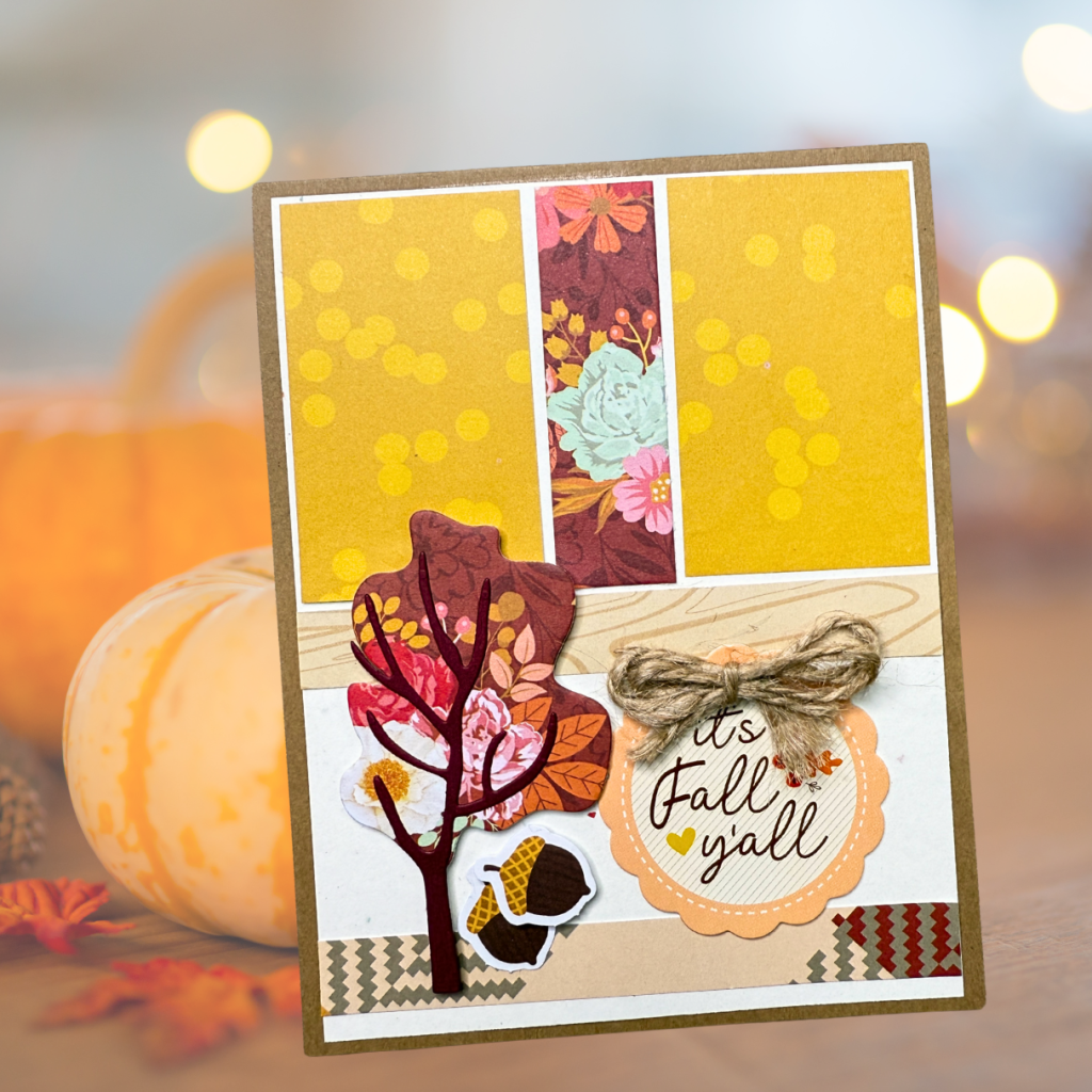 A handmade card featuring a tree with autumn leaves, an acorn, and a sentiment that reads 'It's Fall y'all'. The card has a warm color palette with patterned papers in yellow, floral, and wood grain designs.