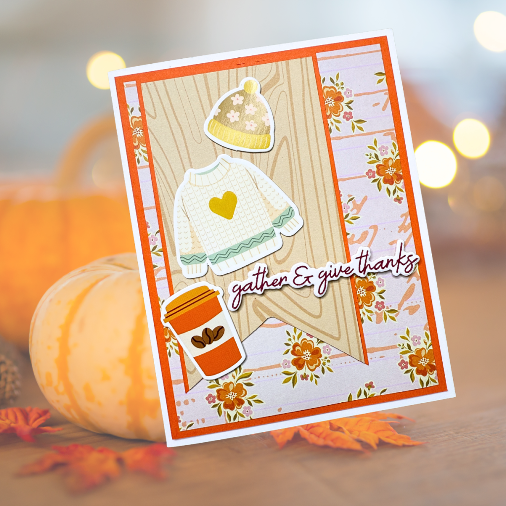 A handmade card featuring a cozy sweater, a hat, and a coffee cup, with the text 'gather & give thanks' on a patterned background framed with autumnal colors.