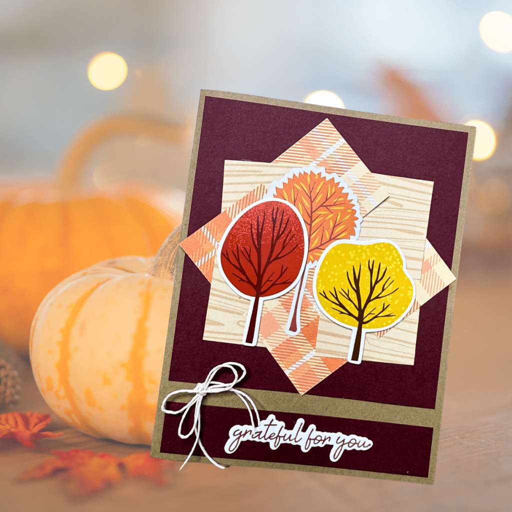 A handmade card featuring colorful autumn trees in red, orange, and yellow, with a background of patterned paper and a sentiment that reads 'grateful for you'.