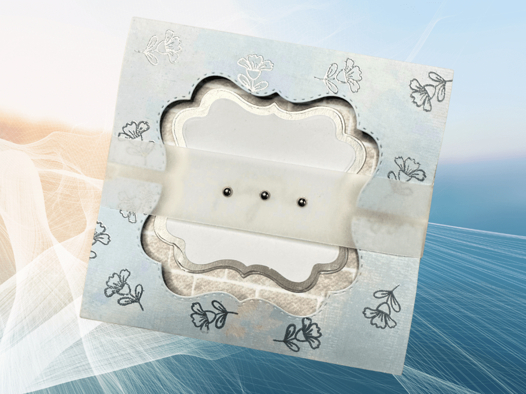 A beautifully designed card featuring a cut-out frame with floral patterns, adorned with a vellum belly band and decorative silver pearls, set against a soft gradient background.