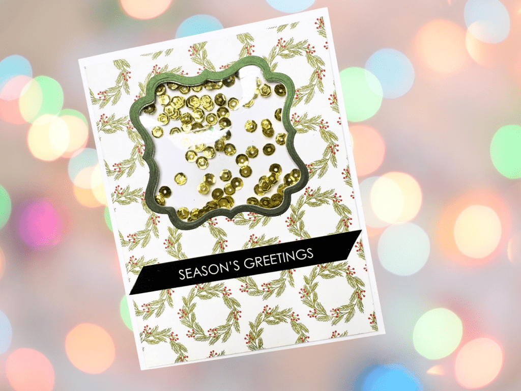 A festive shaker card featuring a patterned background of holly leaves and berries, with a decorative window frame filled with gold sequins and the text 'SEASON'S GREETINGS' on a black banner.