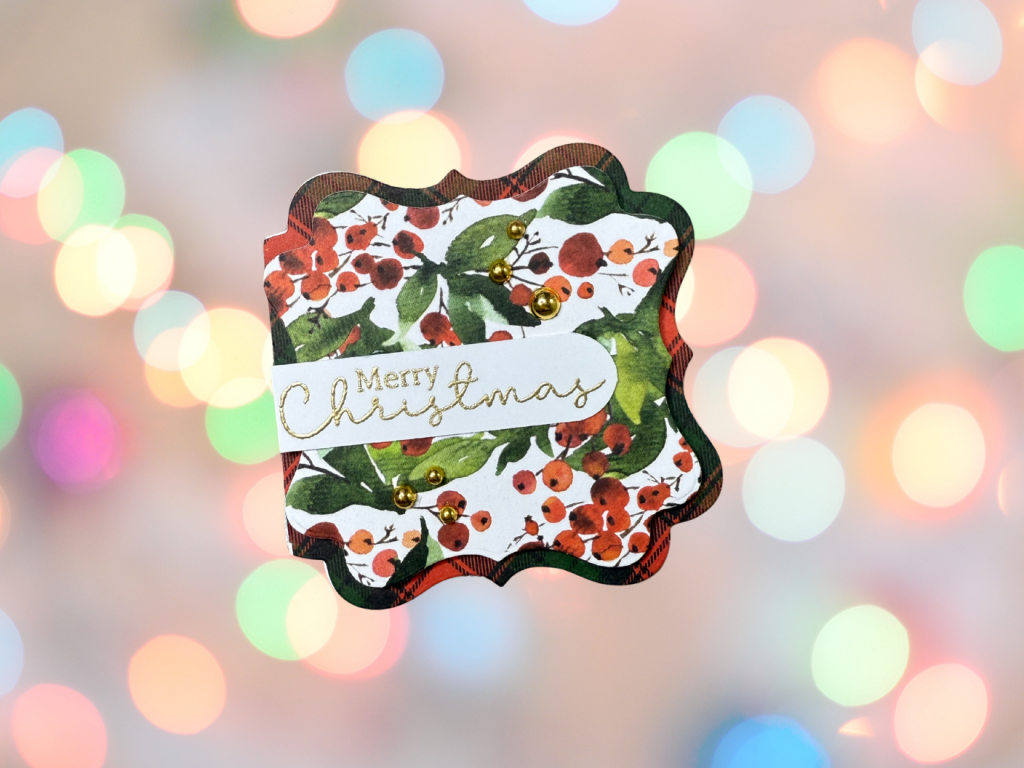 A shaped gift tag featuring a floral design with red berries and green leaves, embellished with gold pearls and a gold-embossed 'Merry Christmas' sentiment.