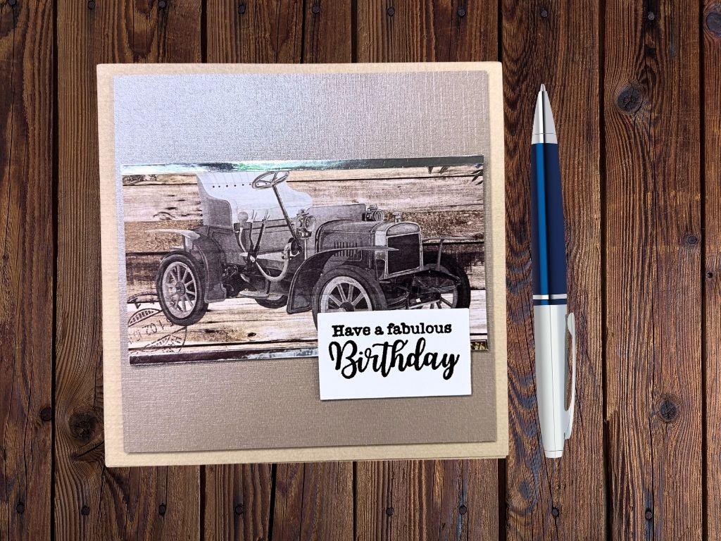 A handmade birthday card featuring a vintage car illustration on a wooden background, with the text 'Have a fabulous Birthday' in a decorative font, placed on a textured gray panel.
