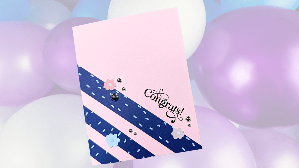 A handmade card with a pink base featuring blue diagonal stripes, decorated with small flowers and jewels, and the word 'Congrats!' prominently displayed.