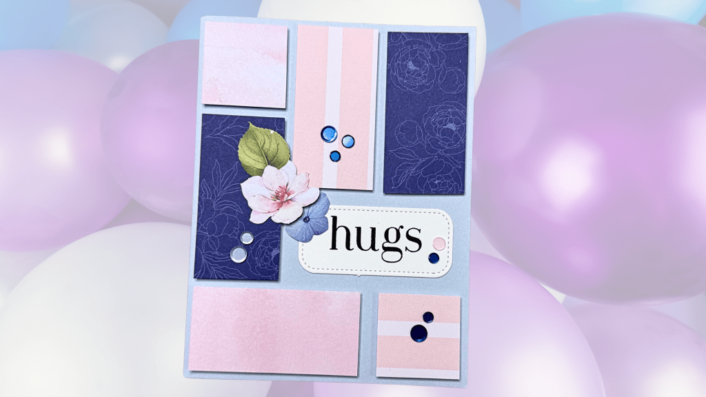 A handmade card featuring a 'hugs' sentiment surrounded by patterned paper pieces in various colors, with floral embellishments and decorative gems, set against a backdrop of soft pastel balloons.