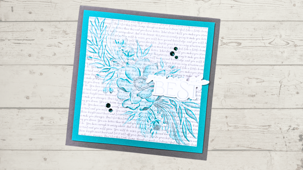 A handmade card featuring an embossed floral design in turquoise, layered on a white background with text, and highlighted with a white sentiment that reads 'BEST'. The card is set against a gray backdrop.