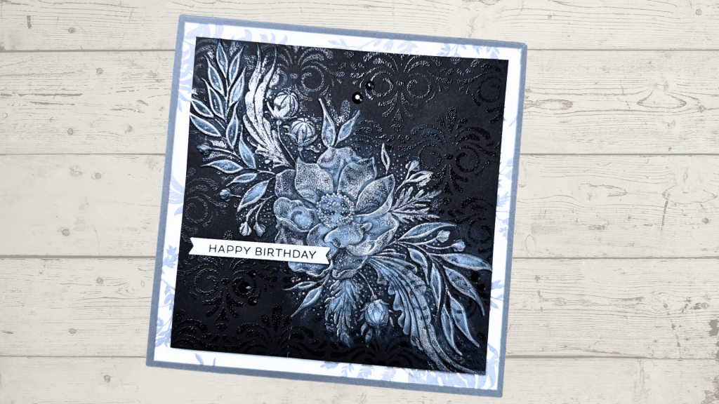 A birthday card featuring an embossed floral design in shades of black and blue, with the sentiment 'HAPPY BIRTHDAY' prominently displayed.