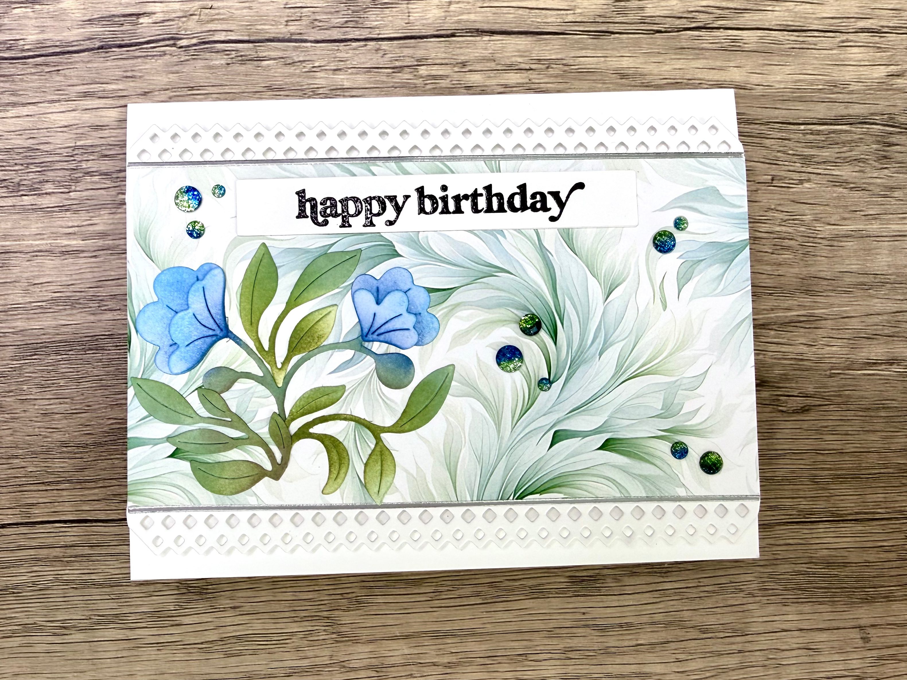 A flat birthday card featuring blue flowers and greenery on a light background, with the text 'happy birthday' prominently displayed.