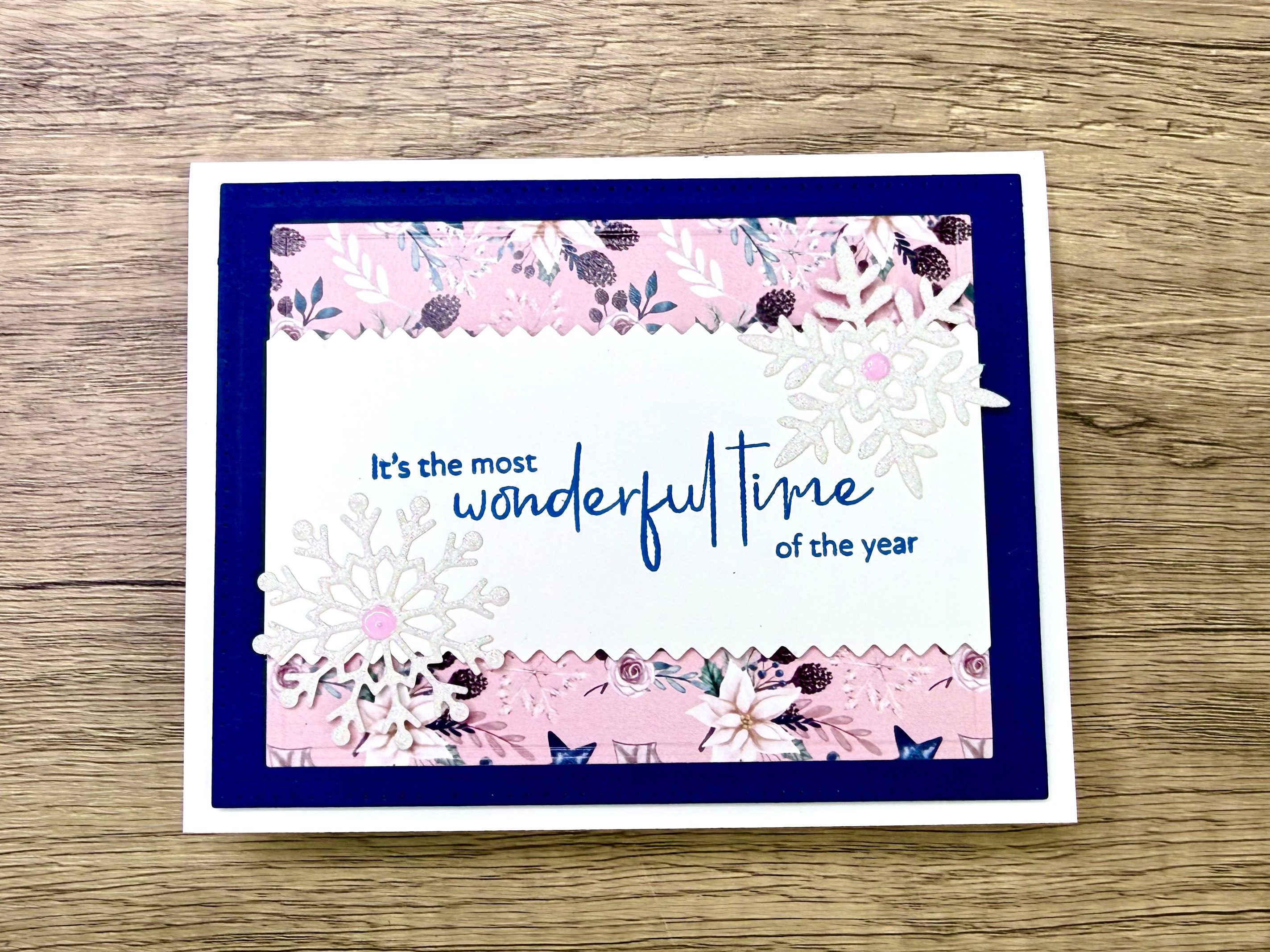 A handmade card with a blue and pink color scheme featuring the text 'It's the most wonderful time of the year' and decorative snowflakes.