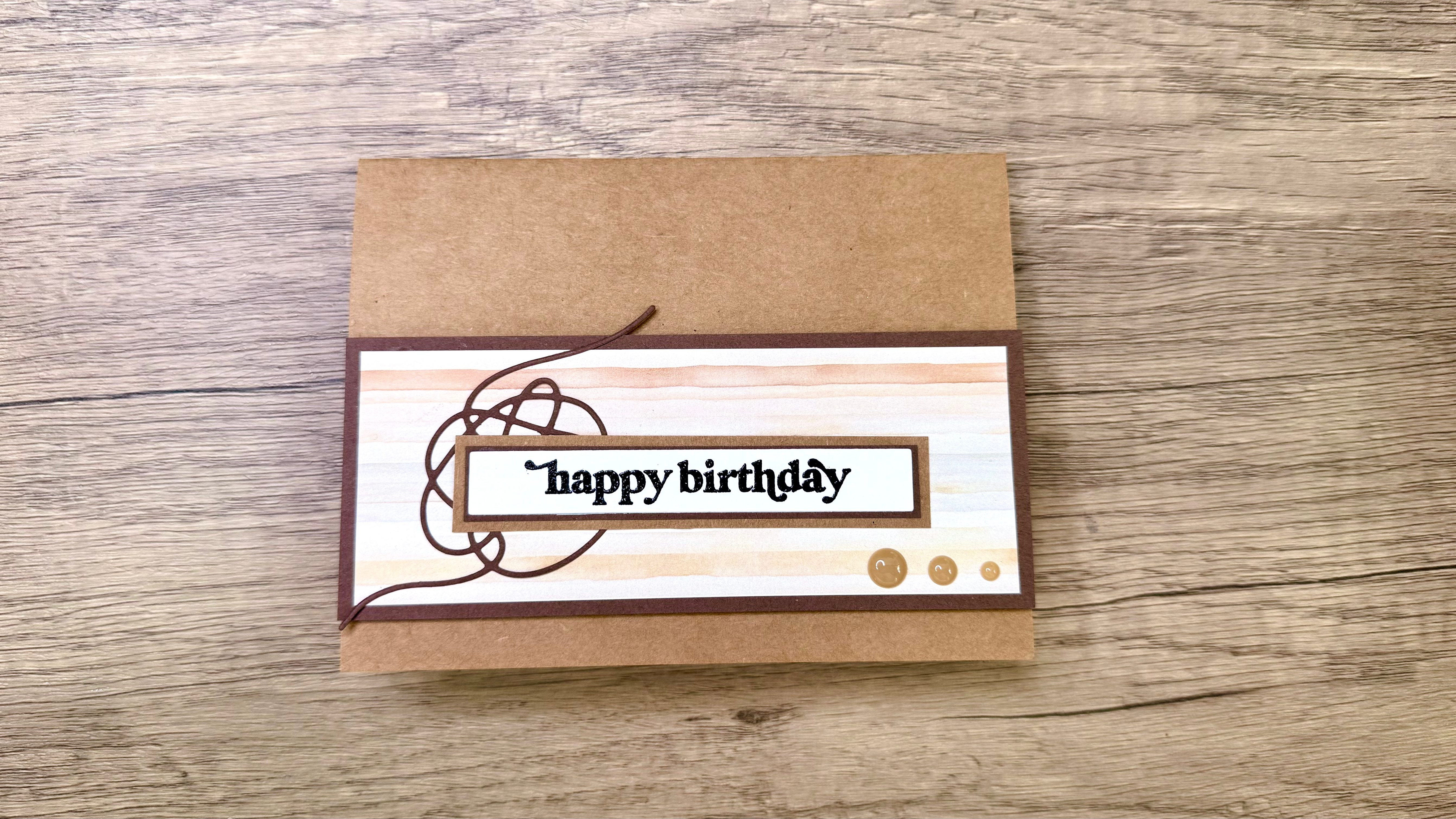 A handmade birthday card featuring a light brown base, a patterned overlay with muted colors, and the text "happy birthday" in a decorative font.