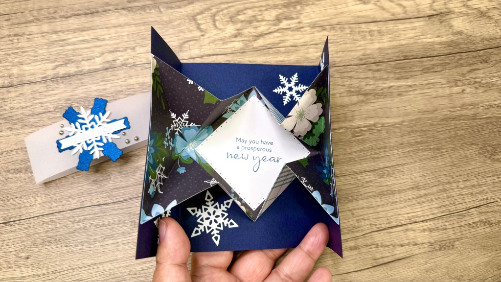 An explosion greeting card featuring a diamond-shaped pop-out center with decorative floral patterns, sentiment reading 'May you have a prosperous new year,' and surrounded by snowflake embellishments.
