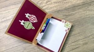 An open holiday card with decorative ornaments inside, a blank space for writing, and a slot for a gift card.