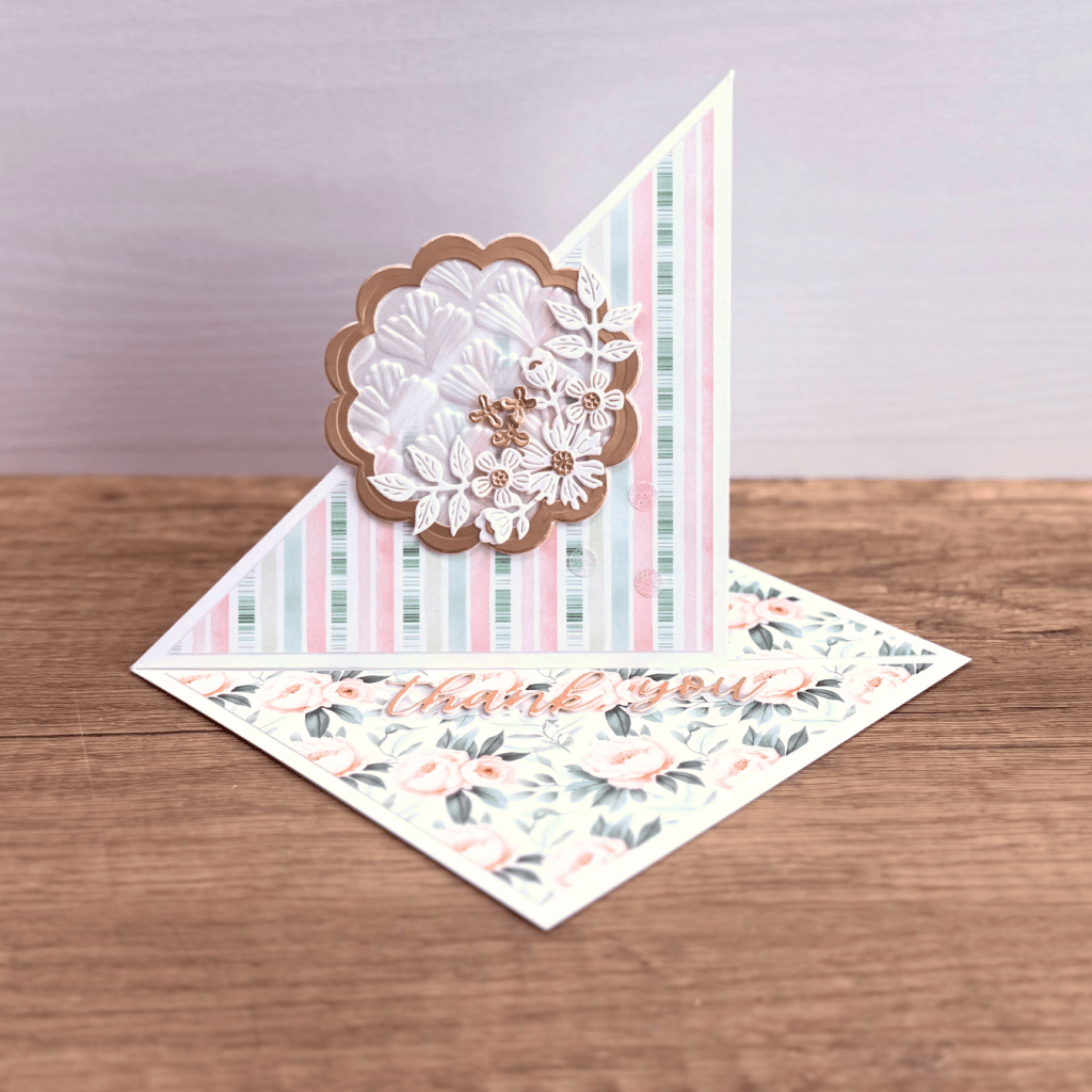 A handmade thank you card featuring a decorative scalloped design, floral embellishments, and pastel striped patterns.