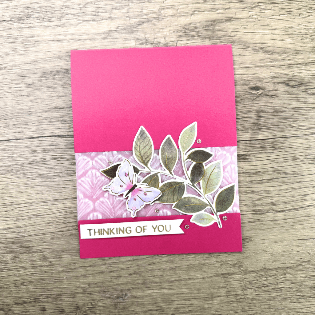 A pink greeting card featuring a decorative butterfly and leaf design, with the text 'THINKING OF YOU' on a white banner.