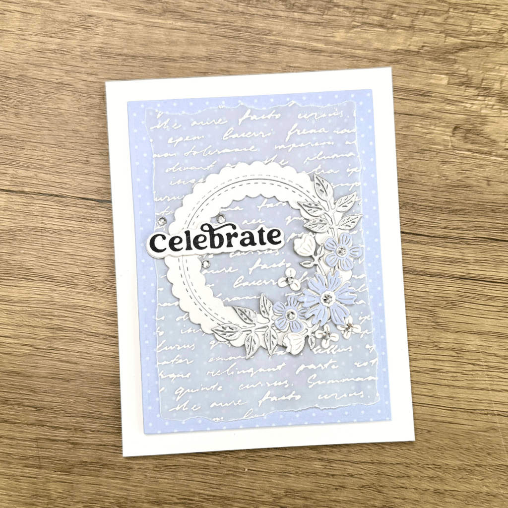 A greeting card featuring a light blue background with handwritten text, adorned with floral embellishments and the word 'Celebrate' in bold typography.