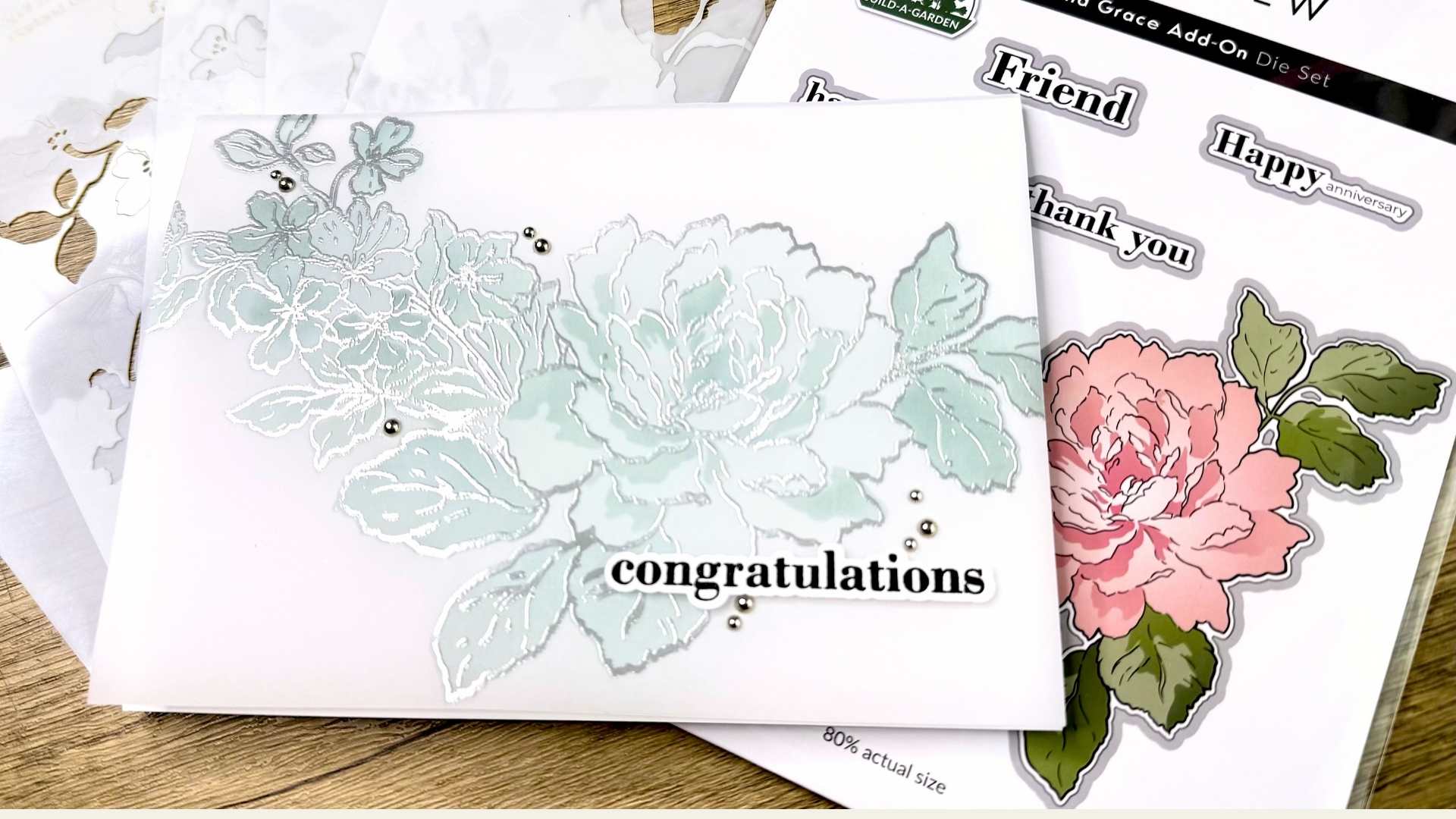 Vellum greeting card made with Altenew products with heat embossed floral design in pale blue and silver and congratulations sentiment on wooden table