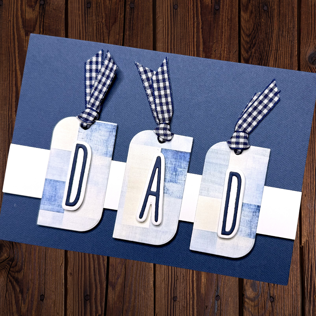 Blue and white tags with letters spelling DAD, each tied with blue checkered ribbon on a blue card