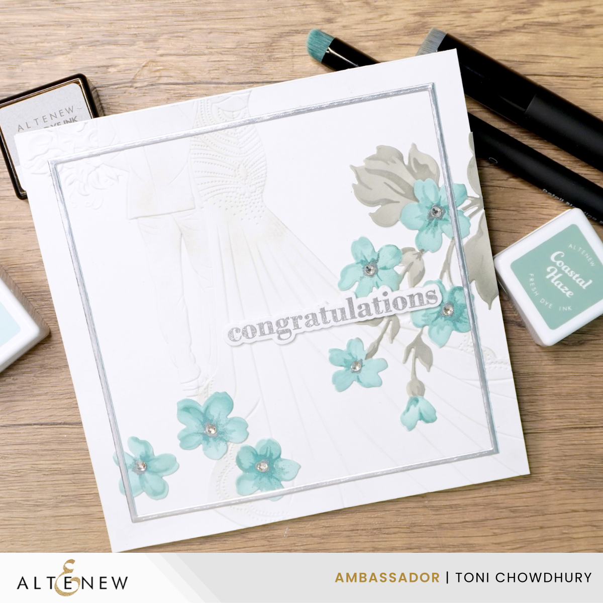 HandmadeCardsByToni-EnchantedBeginnings-HillBlossoms-1 White congratulations card with embossed bride and groom, blue flowers with rhinestones, surrounded by stamping ink pads and brushes