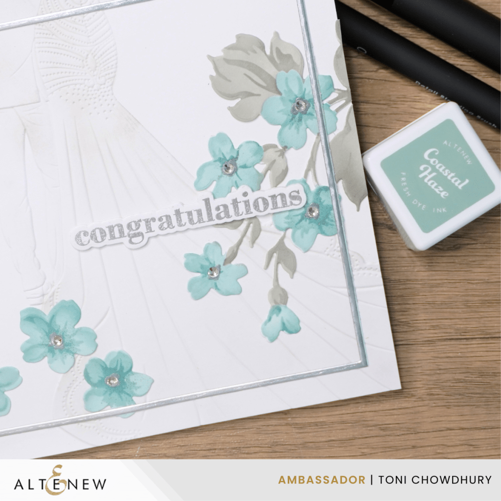 White congratulations card with embossed bride and groom, blue flowers with rhinestones, surrounded by stamping ink pads and brushes