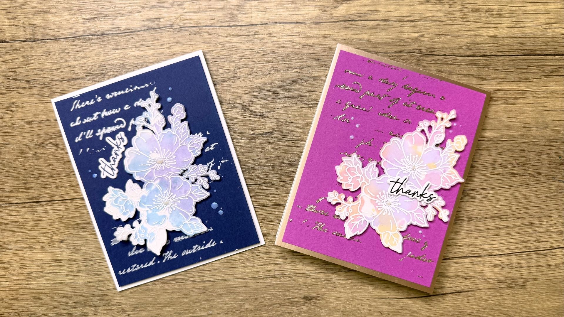 Two handmade thank you cards with floral designs on a wooden surface, one with a navy blue background and the other with a purple background
