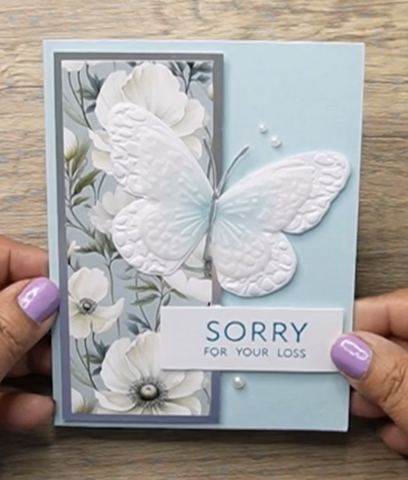 Sympathy card with large embossed white butterfly, floral pattern, and text saying Sorry for your loss